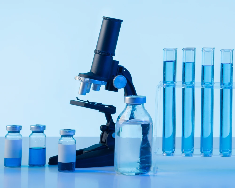 Grafika kategorii mikrobiologicznych badań wody przedstawia mikroskop i fiolki z wodą do badań w niebieskiej scenerii.