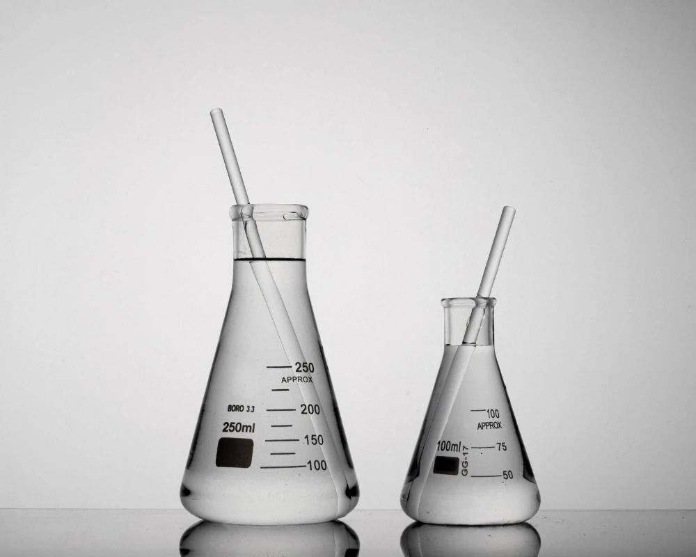 Grafika kategorii fizykochemicznych badań wody przedstawia kolby stożkowe z wodą w laboratorium badań wody.